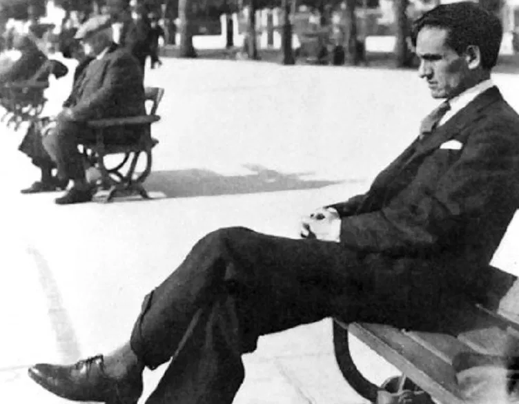César Vallejo seated on a park bench in a dark suit, legs crossed, looking aside