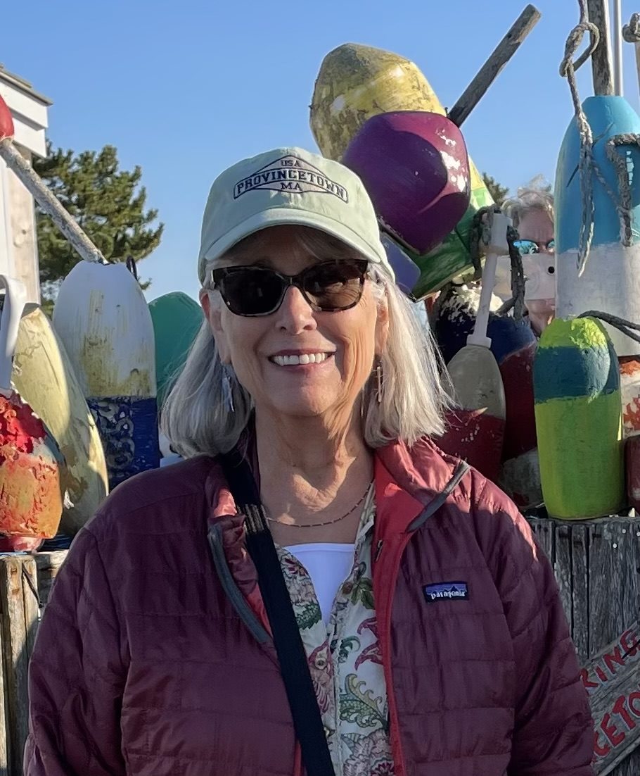 Cathryn Shea in a Provincetown cap, standing before a stack of painted buoys