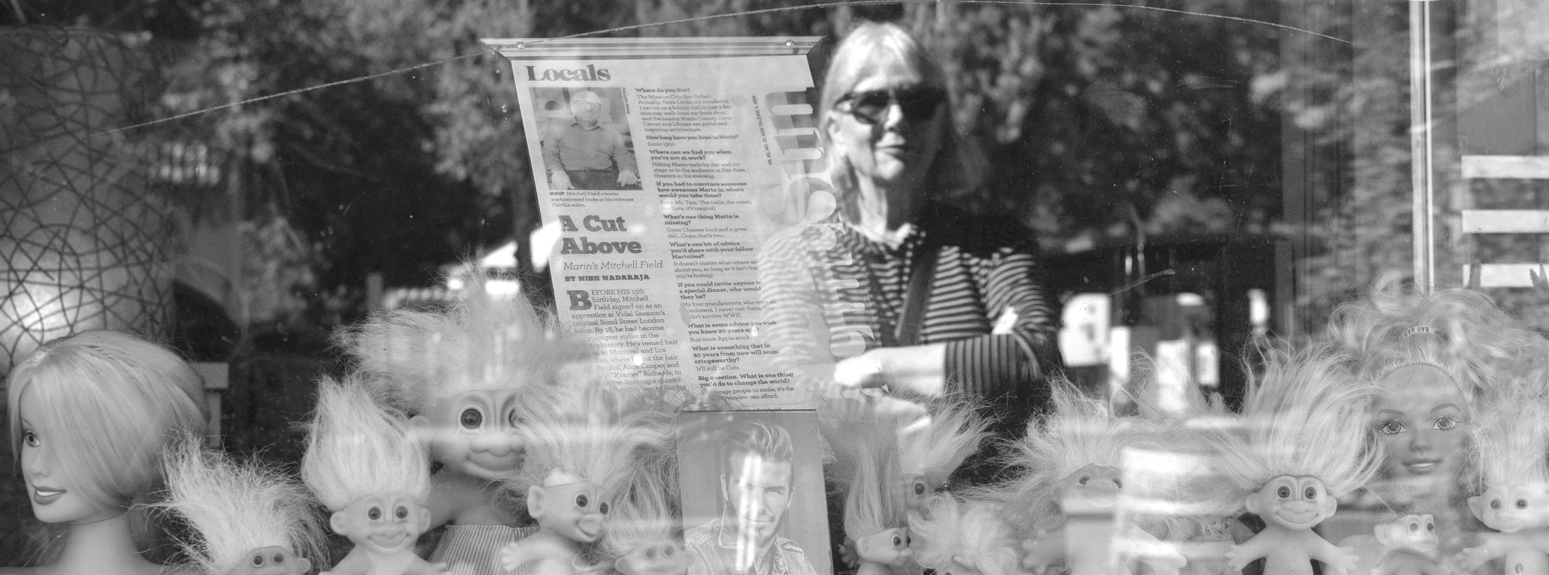 Cathryn Shea seen through a shop window, among troll dolls and a posted page