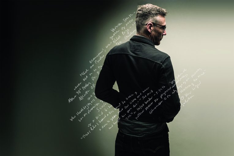 Gabriel Gudding seen from behind, handwritten lines crossing the dark field around him