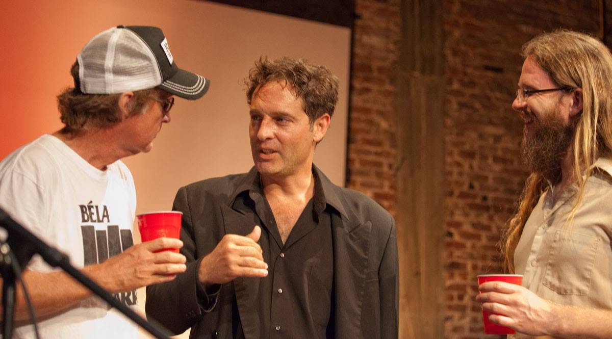 Three men talking after a reading, one holding a red cup